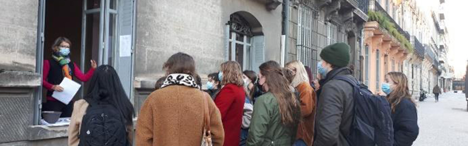 Students are gathered in a semi-circle outside and are listening to their instructor. They are focused and facing away from the camera.