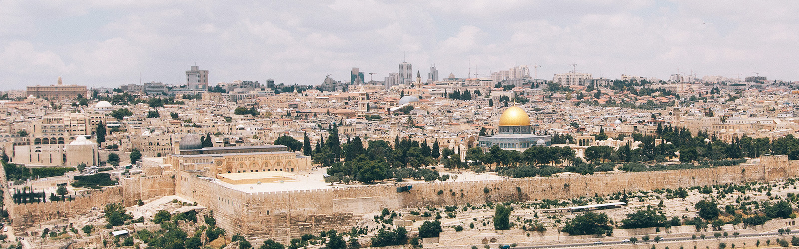 A city skyline with many tan buildings and one taller gray building with a golden dome in the center. 