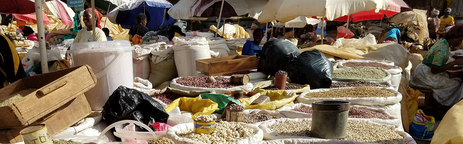 Various bags of nuts and seeds are at a busy outdoor market.
