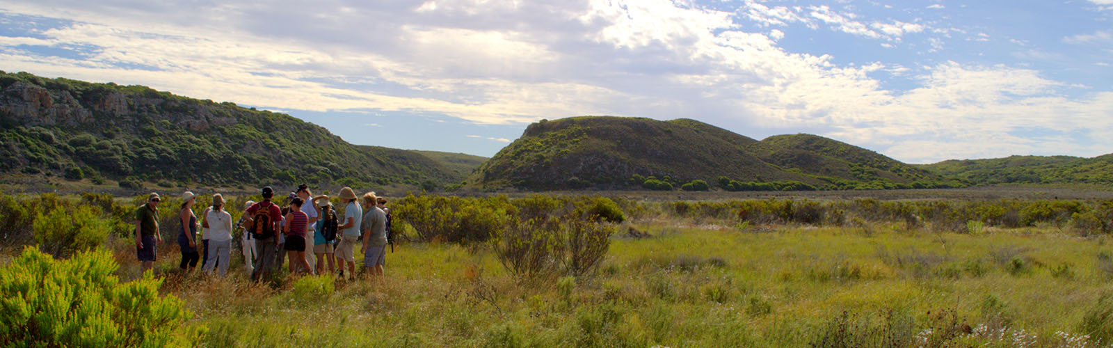 Students gathered on a grassy plain, with hills in the background, on a sunny day.
