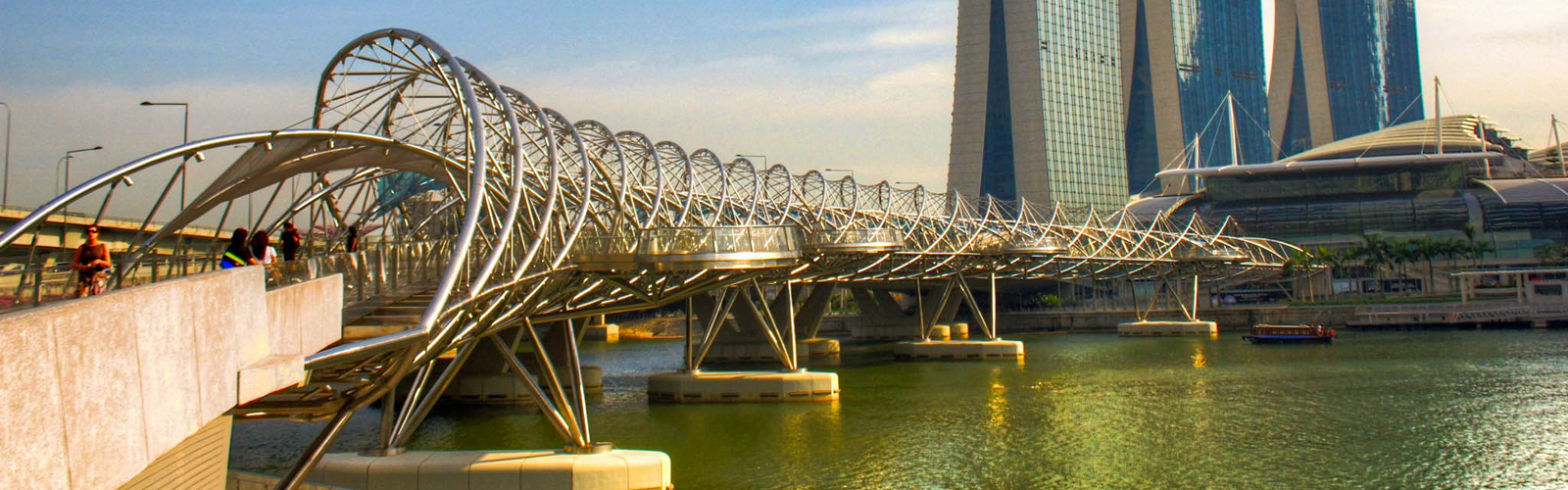A modern pedestrian bridge of curving metal over water near the Marina Bay Sands towers.