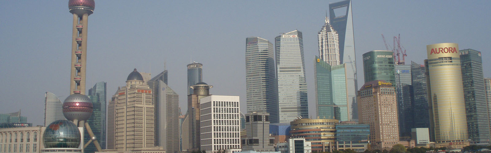 View of the Shanghai skyline from the water on a cloudy day. The fog blocks some of the view of the large buildings.