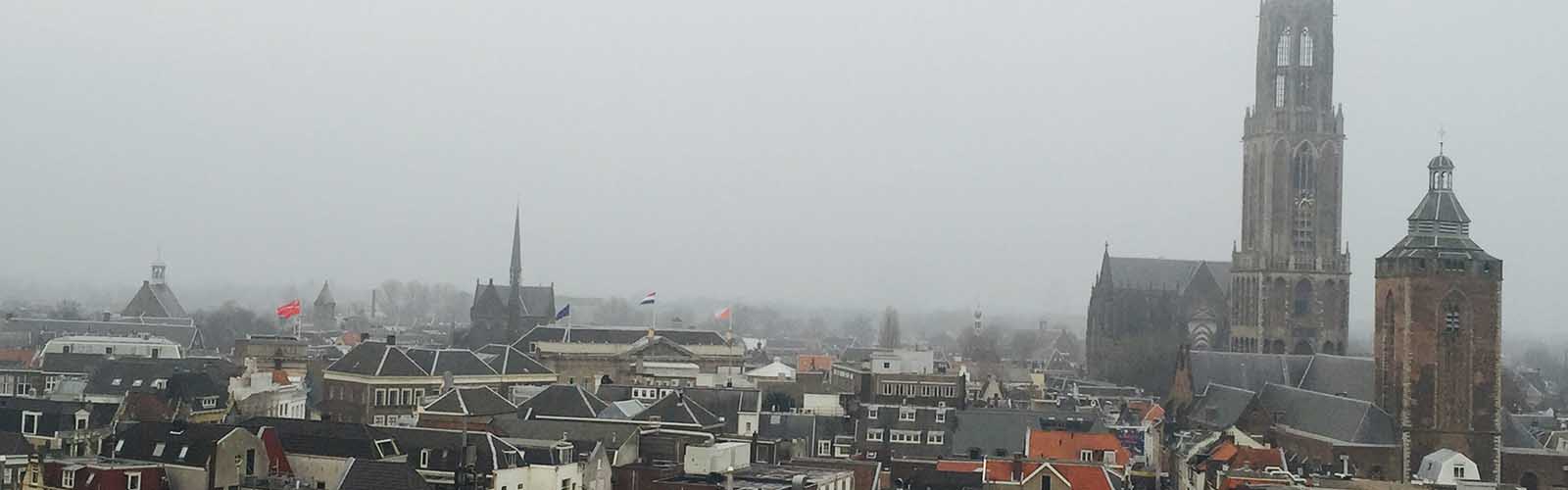 A high-up view of a city with orange and gray buildings on a foggy day. A tall church spire is on the right. 