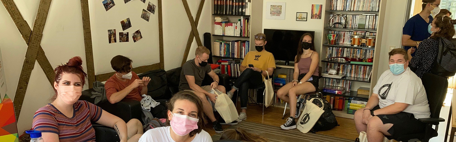 Students are gathered together and hanging out in a common area. Some students are smiling at the camera and others are chatting with each other.