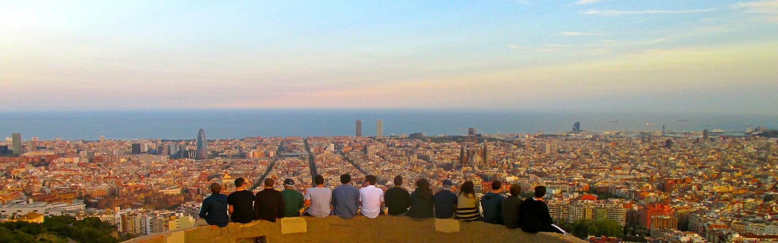 Fourteen individuals sitting at an overlook, with Barcelona sprawling across the background.
