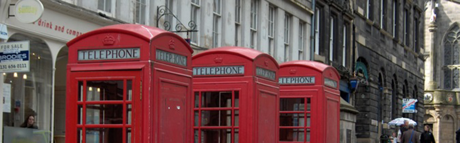 Three iconic red phonebooths in aline alongside a busy street.