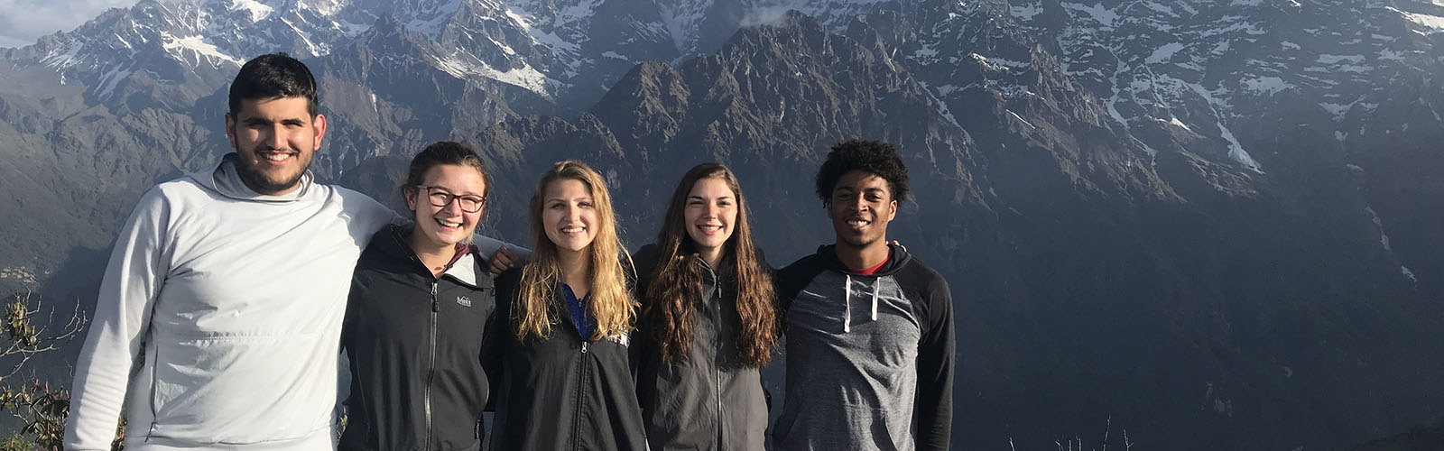 Five students stand in front of a snow-covered rocky mountain. 