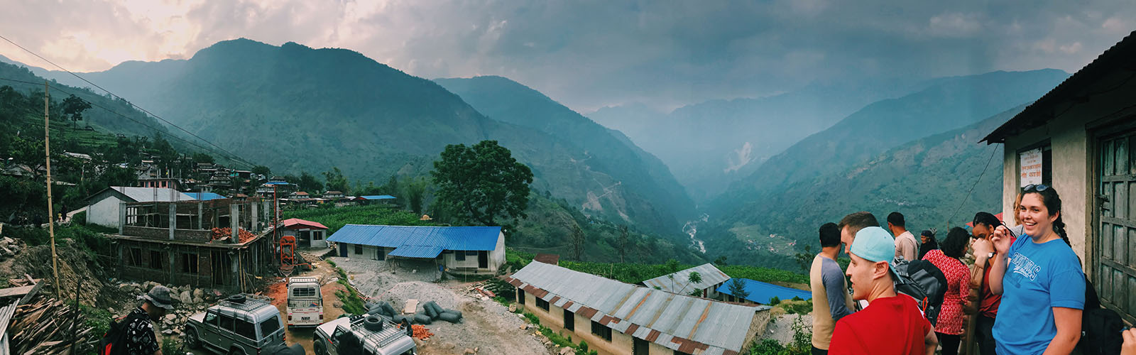 Students stand outside of a building and overlook the many green mountains in the distance. 