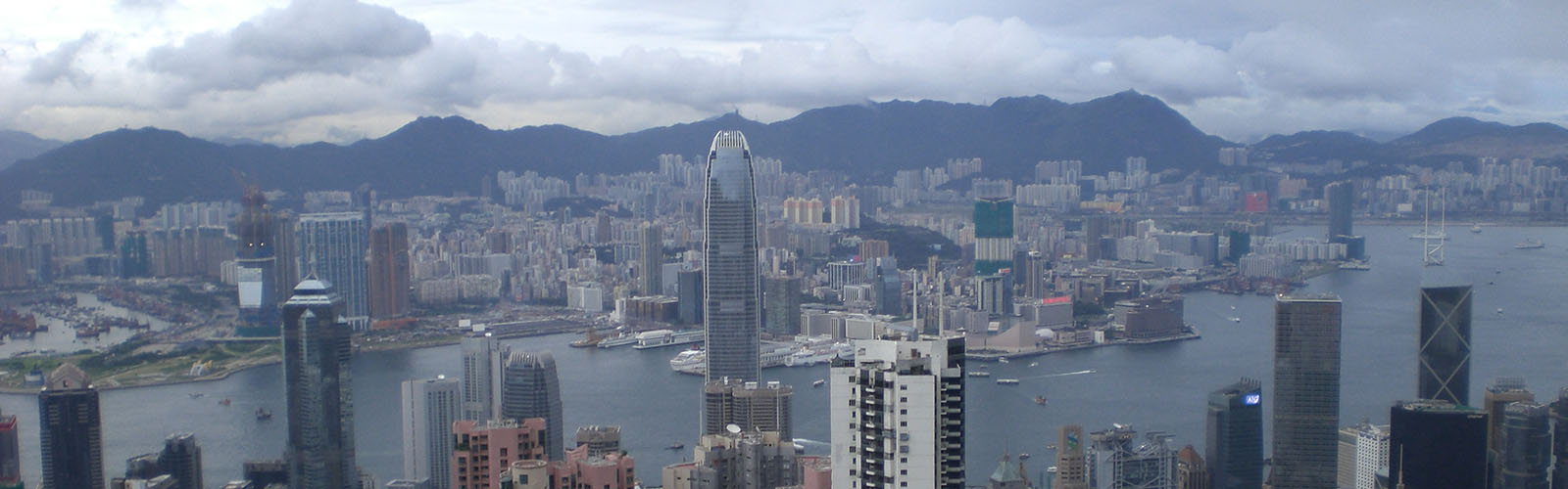 The skyline of Hong Kong, featuring a river with skyscrapers on both sides of the river, and mountains in the distance. 