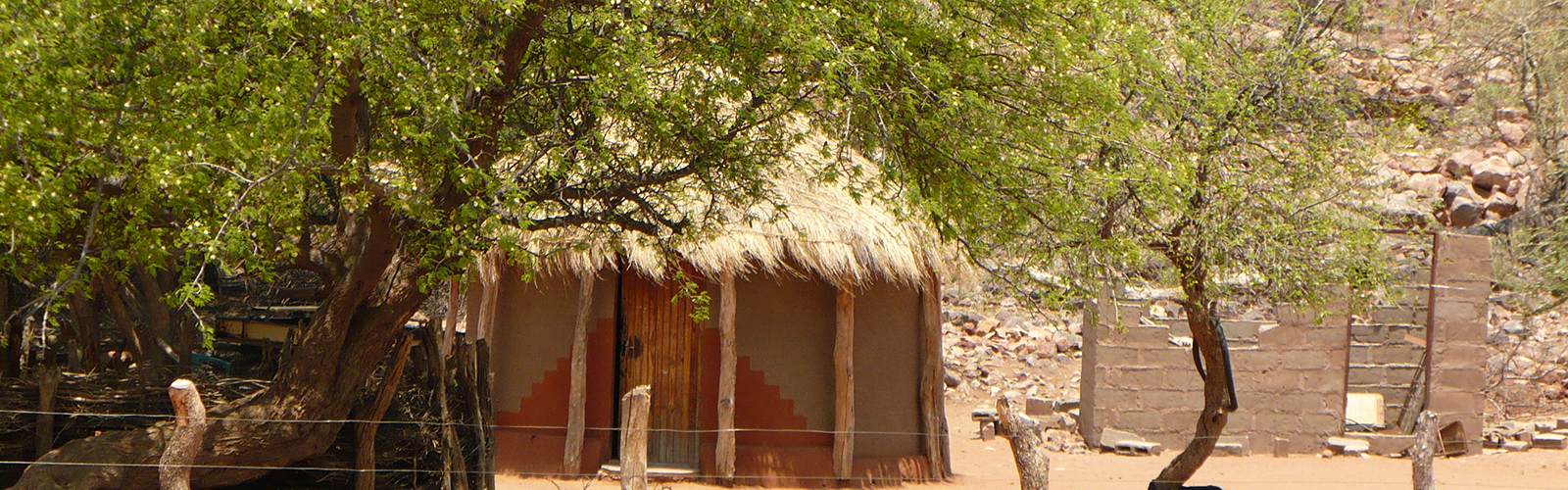 A village house is surrounded by desert and few trees.