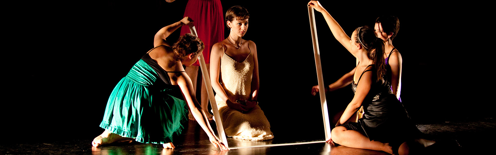 Four students acting in a performance. They are on a dark stage and dressed in minimalistic costumes.