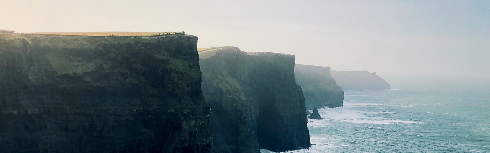 Several cliffs have turquoise blue waves crashing up onto them. 