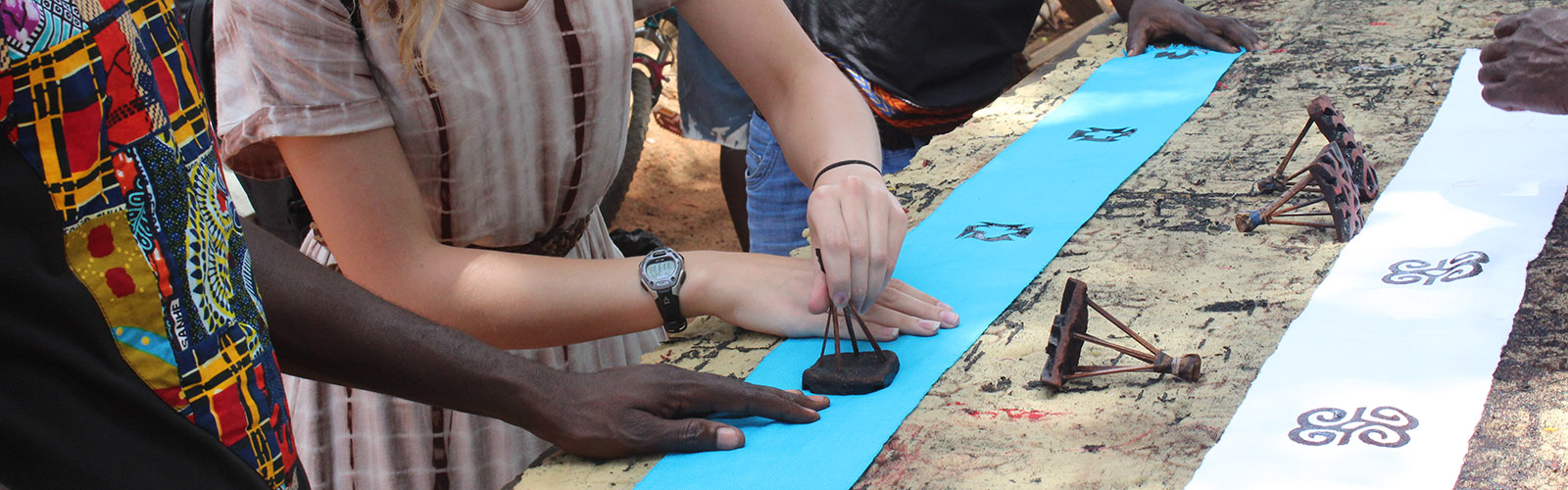 Two people are using stamps to add patterns onto various pieces of fabric. Only their hands are visible.