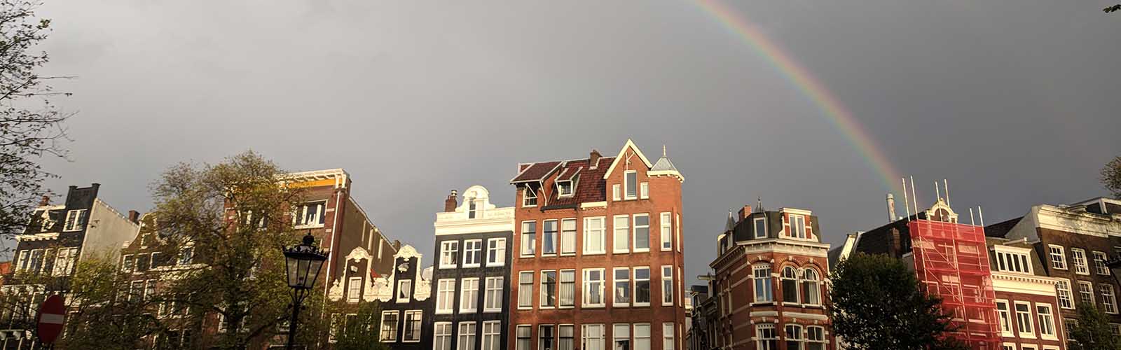A rainbow is visible behind a street of tall, narrow, brick houses.