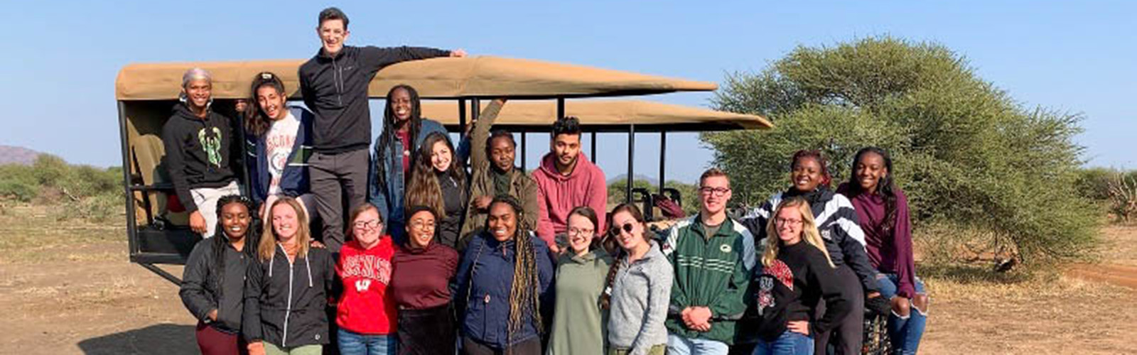 Students are gathered around a safari vehicle and are all smiling at the camera