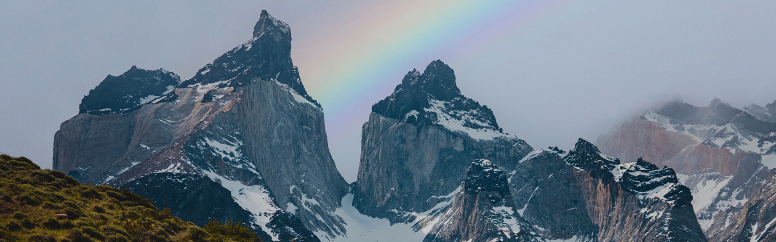 Two mountain peaks with snow on them. A rainbow passes between the peaks and fog is clouding the background