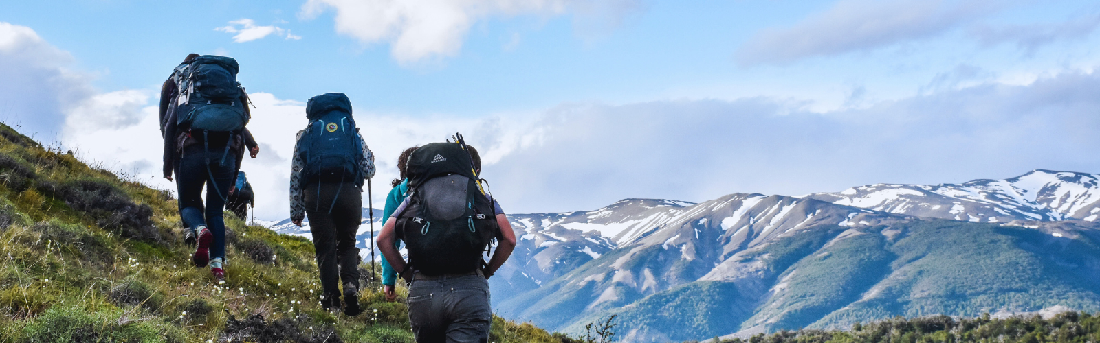 3 backpackers are hiking in the mountains. a long mountain range is in front of them