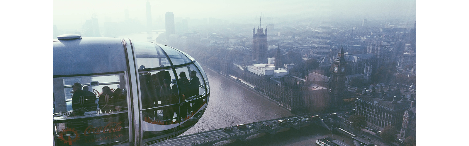 View of a London Eye carrige with the city of London in the background. A dark fog clouds over some of the city.