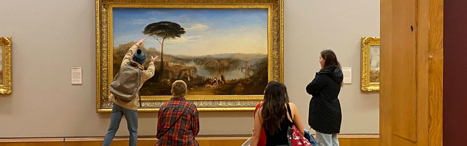 An instructor is teaching students about an art piece. They are all focused on the piece and listening attentively.