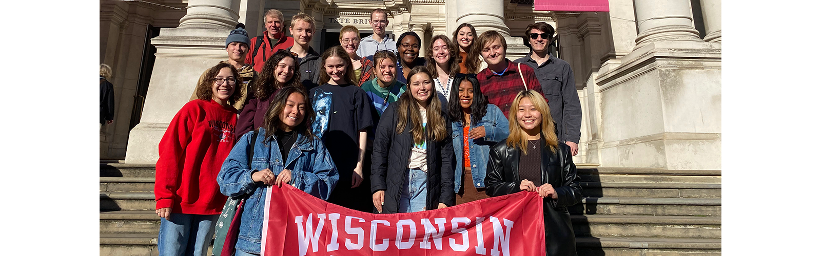 Students are outside of the Tate Britain and holding up a Wisconsin flag. They are all smiling at the camera.