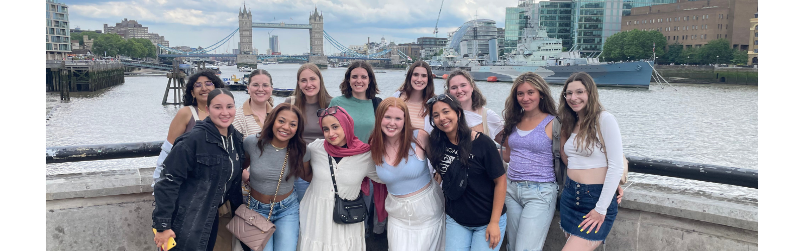 Students are gathered at a photo point near Tower Bridge. They are all hugging and smiling at the camera.