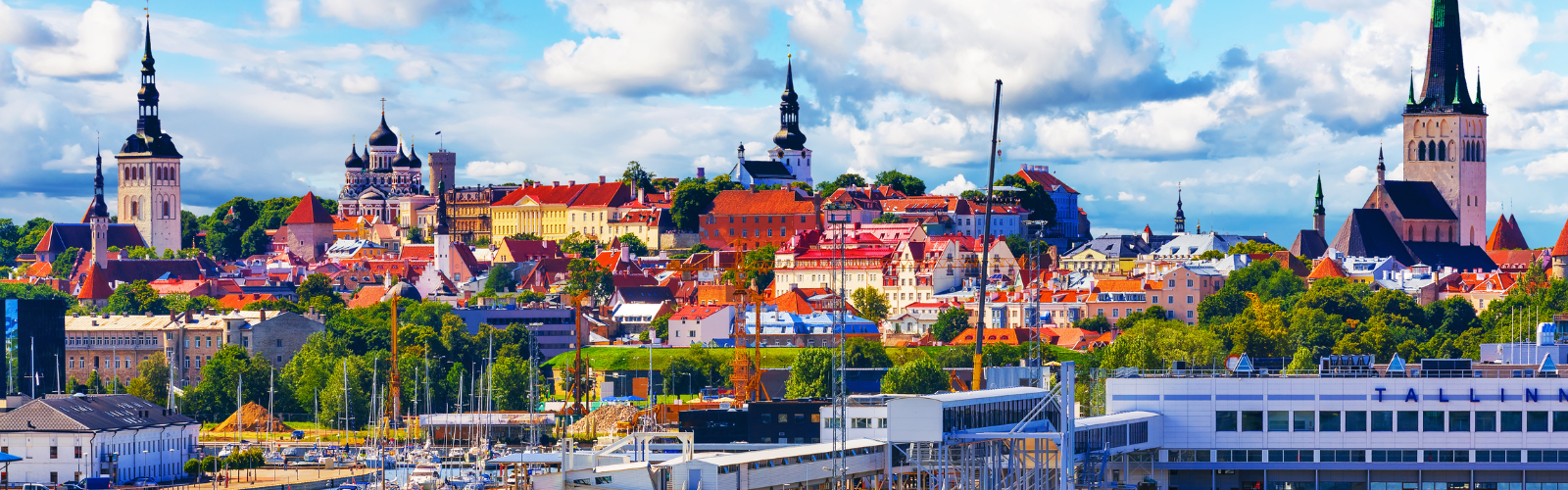 Panoramic view of a Talinn, Estonia, with a mix of colorful historic buildings and church spires under a partly cloudy sky.