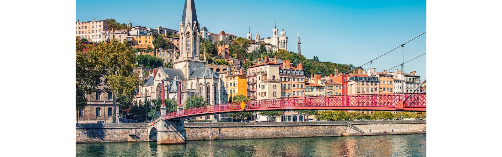 View of the Lyon skyline from the river. A bridge is in the foreground with cathedrals and residential buildings escalading the hill.