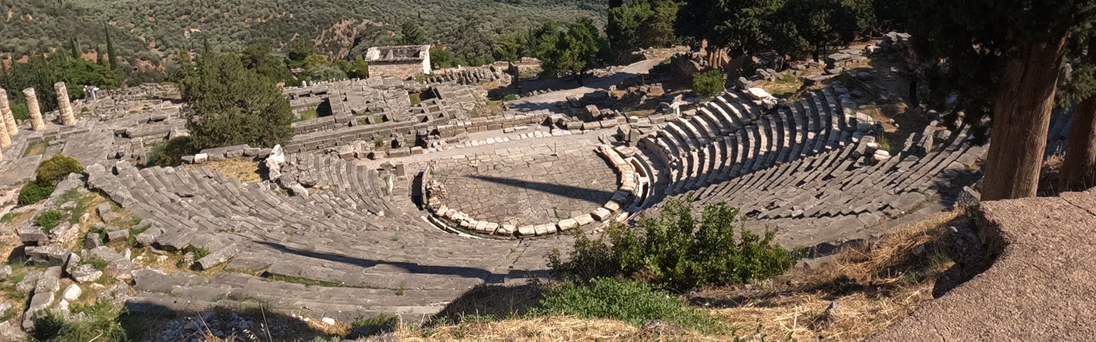 Overhead view of a Greek amphitheater. It is slightly worn down, but still has many rows of seats and a visible stage area.
