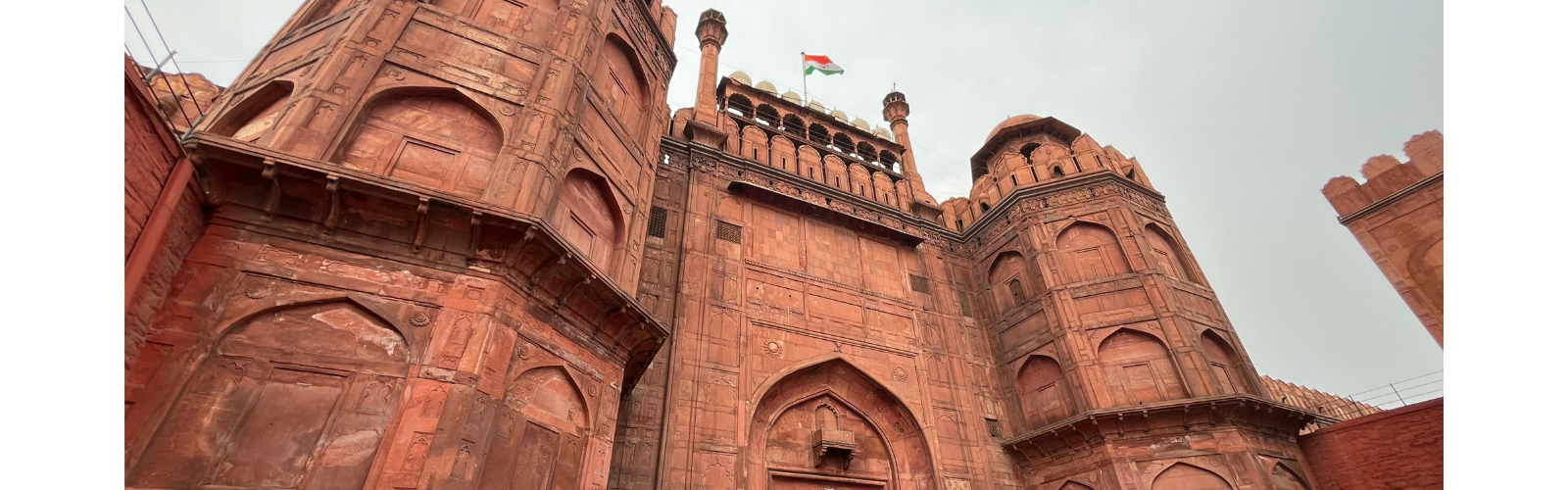 An ornate, orange-brown stone building with many arches and the Indian flag hanging at the top.