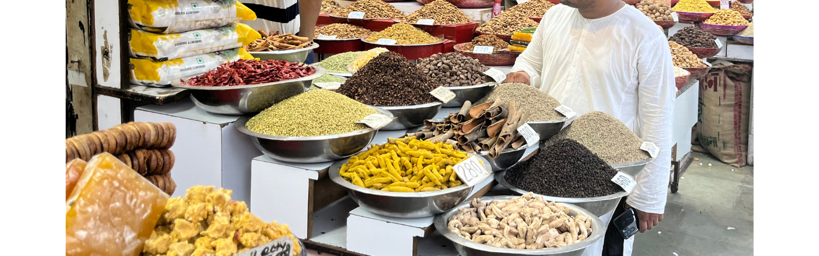 Many large, silver bowls are overflowing with food of all different colors, on display with price tags. 