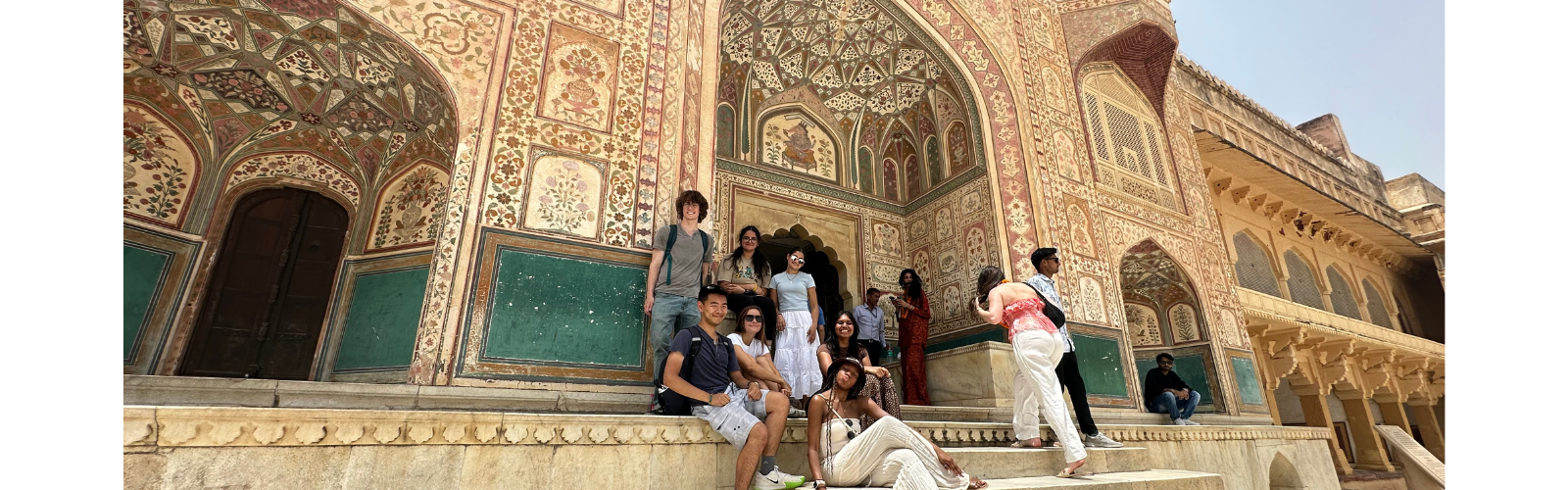 Ten students pose in front of a stone building with intricate patterns.