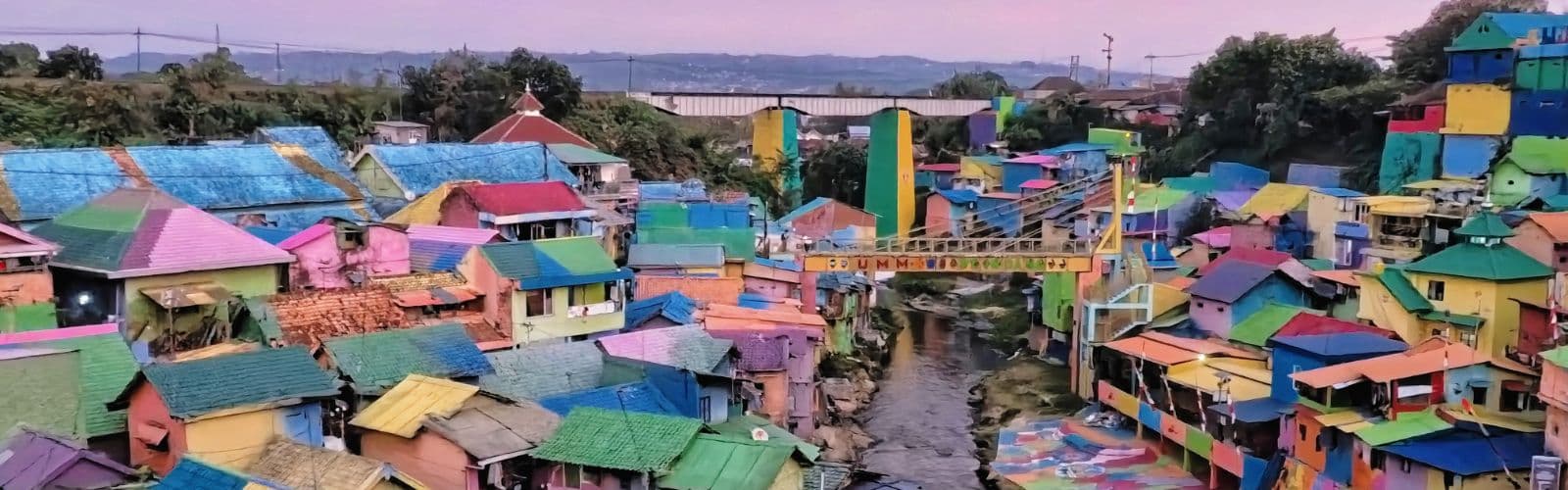 A group of brightly colored houses next to a river at sunset. 