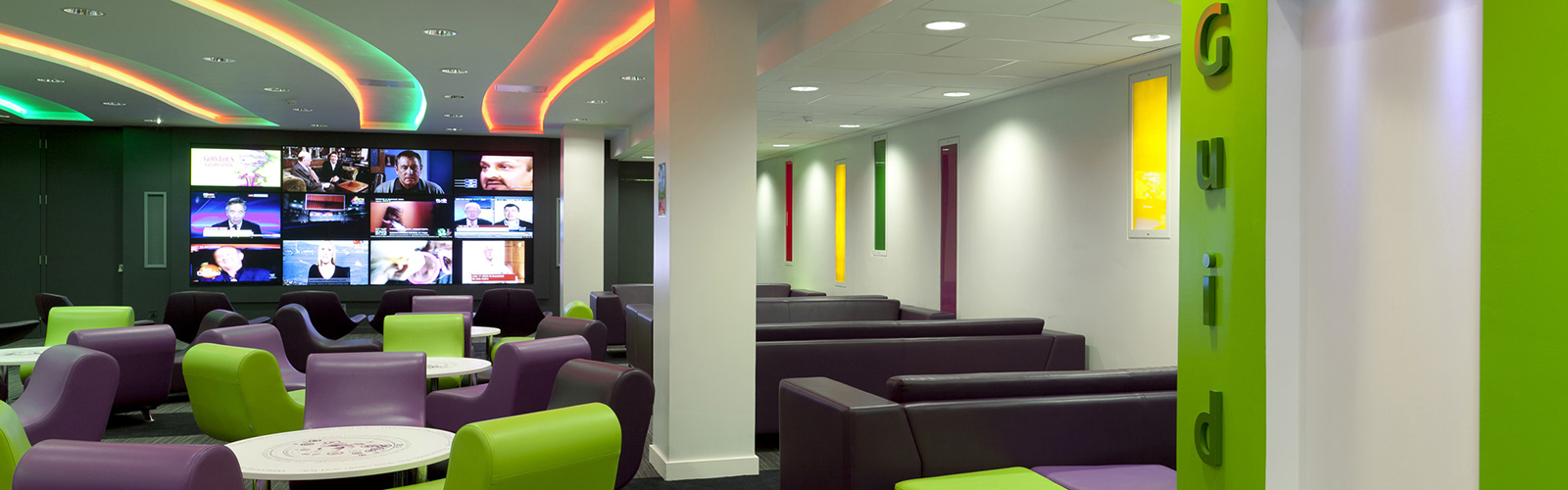 A modern lounge with comfy purple and lime chairs and a large screen. 