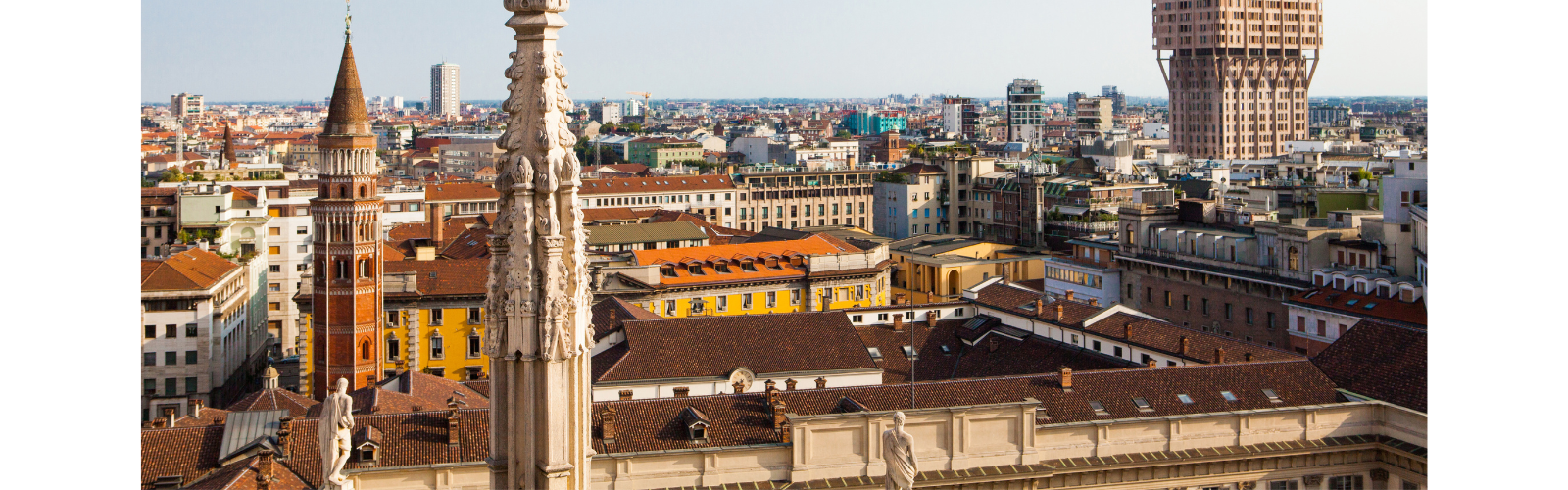 A city skyline with a mix of buildings with dull and vibrant colors. Although many of the buildings are around the same height, some thin, tall spires break up the monotony. 