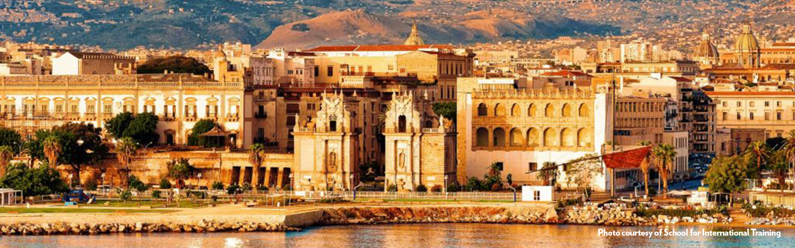 Old stone buildings lining a waterfront, with building-covered hills in the background.