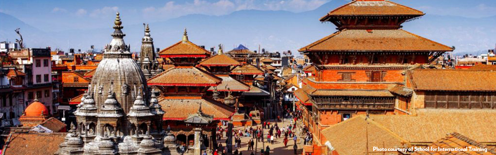 A cityscape with many orange buildings with tiered roofs. Mountains are barely visible in the background. 