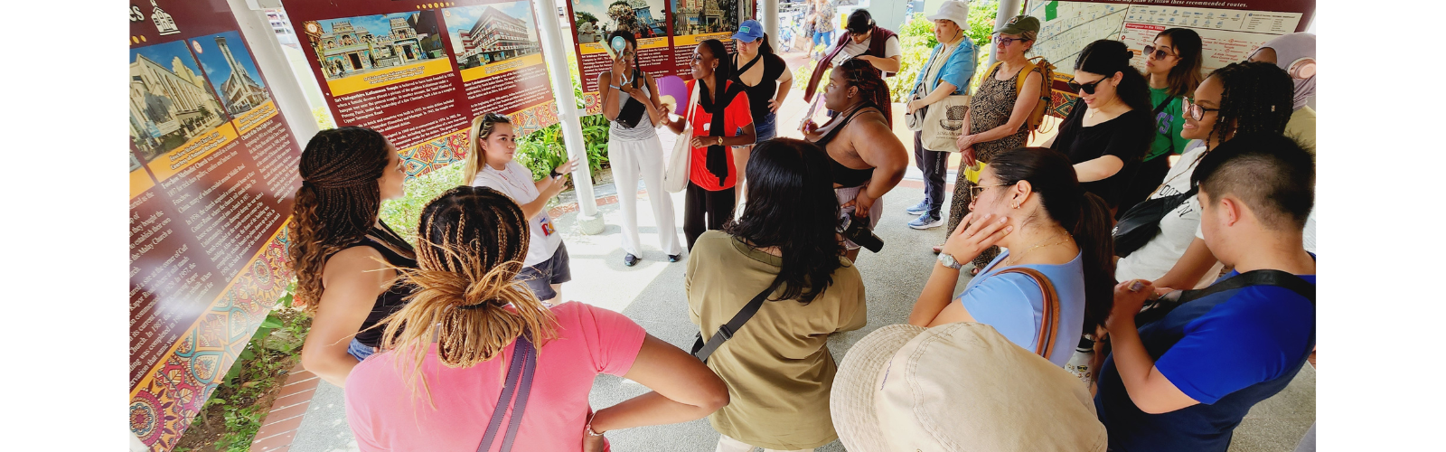 Students and a guide gathered under a pavilion during a walking tour.