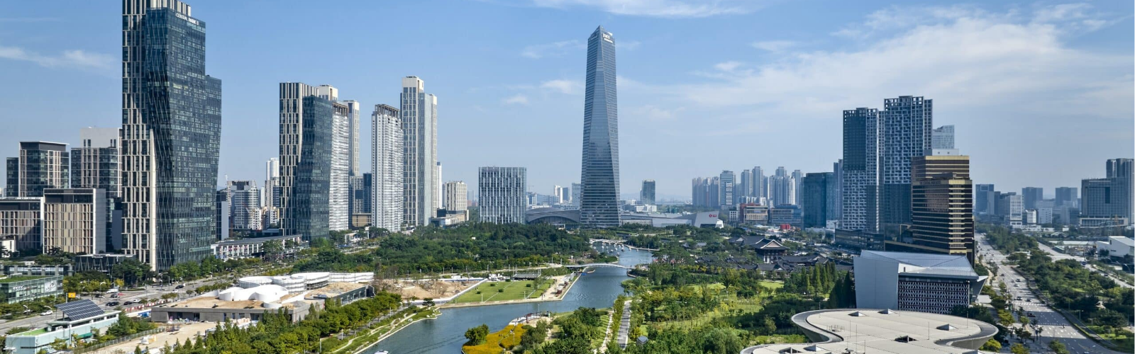 Panoramic view of a modern city skyline with tall, sleek skyscrapers, a central winding river, and lush green parks under a clear blue sky. 