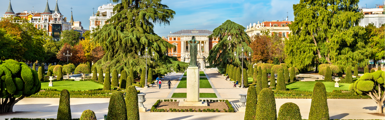 A statue on a pedestal centered in a landscaped park in Madrid, with the Casón del Buen Retiro building in the background.