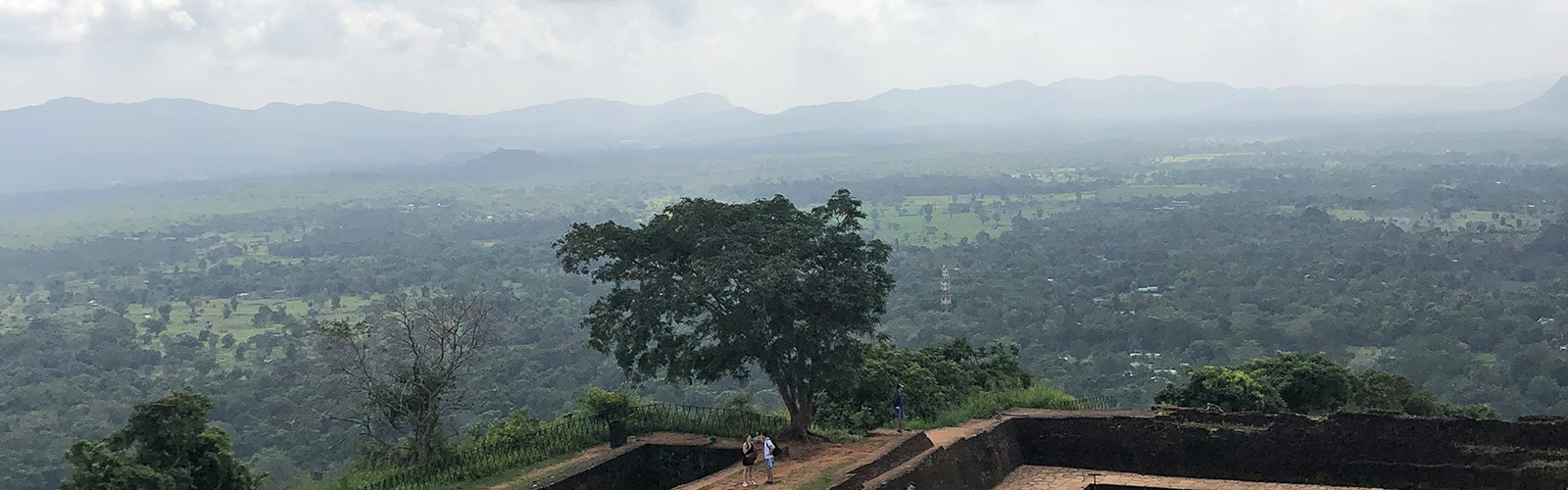 The foundation of an old stone structure, near the top of a hill, with a panoramic view of a valley and hills in the distance.