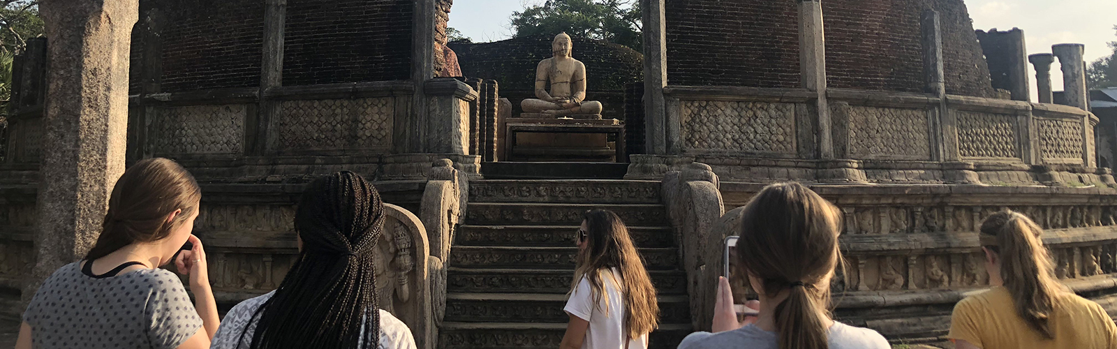 Five students at an old temple, standing near steps that lead to a statue of someone seated.