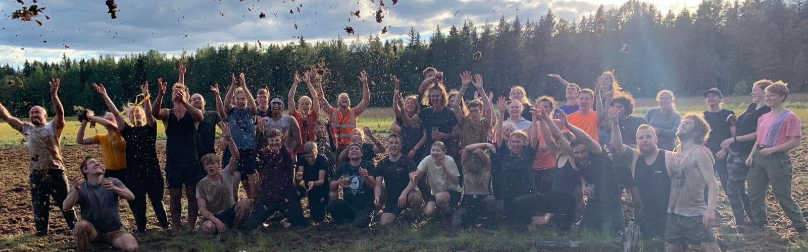A group of students standing in a field throw up dirt into the air on a sunny day. 