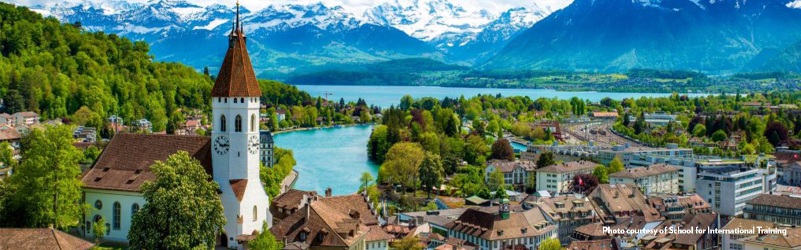 An aerial view of the city of Bern, with water and mountains in the background.