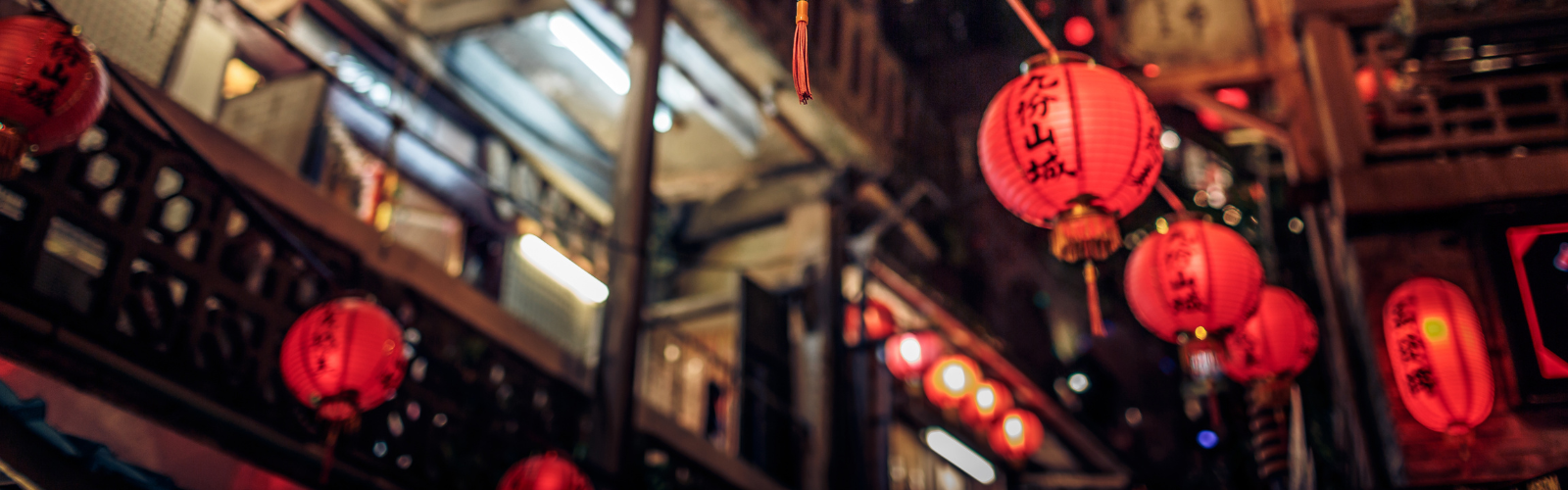 Red lanterns, with black characters on them, hanging along a street at night.