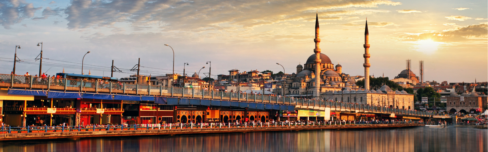 Sunset view of Istanbul's Galata Bridge, bustling with people. The New Mosque stands prominently in the background.
