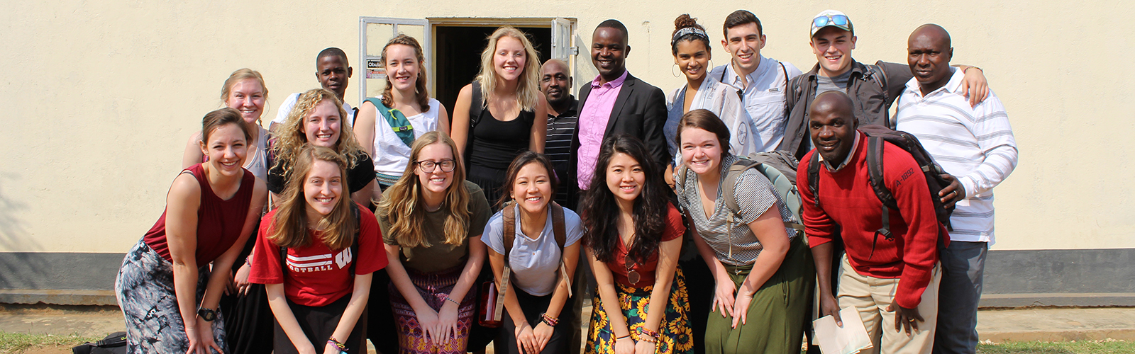 Program participants and other individuals posed in two rows in front of a beige wall.