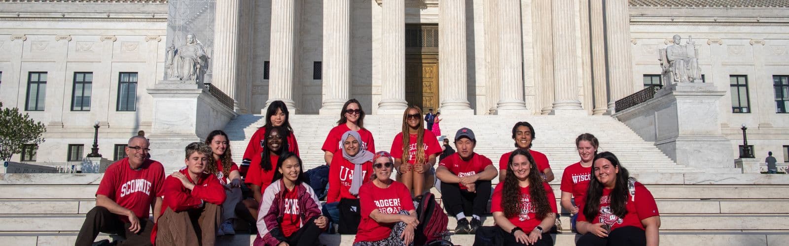 A group of students wearing matching red "Badgers Abroad" shirts sit on the steps of the United States Capitol