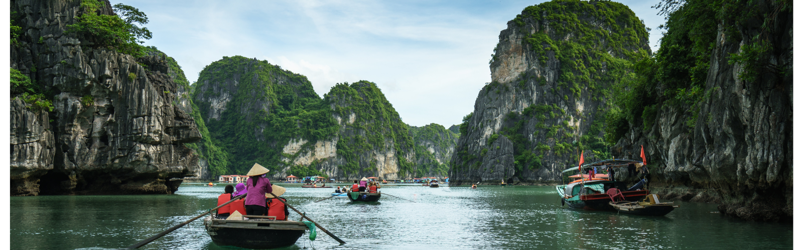 Small boats being rowed along steep, rocky cliffs.
